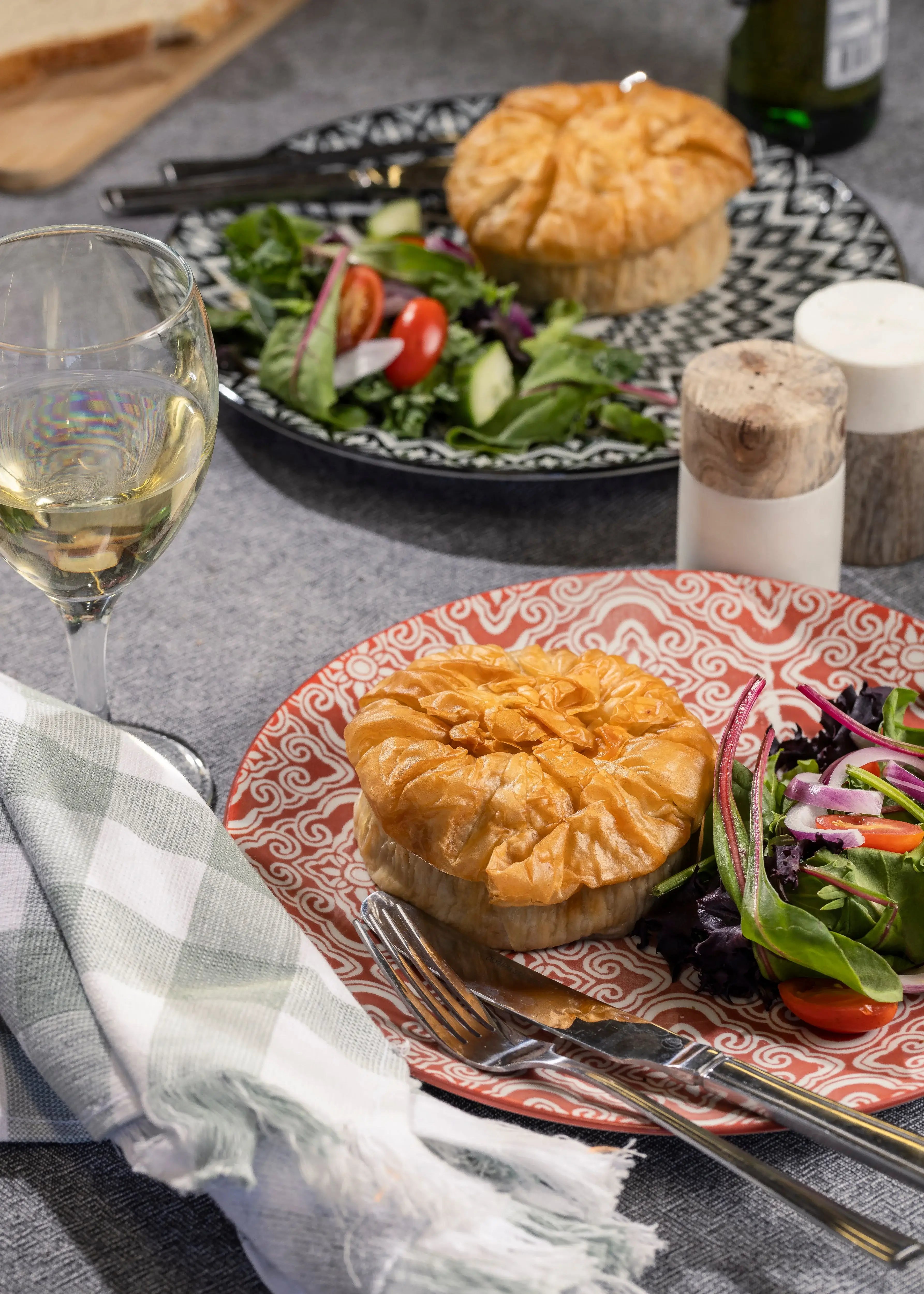 Two dinner plates with Beef & Vegetable Filo Pies and salad sit on a table