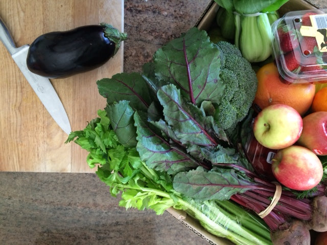 Box of fresh fruit and vegetables on a kitchen bench with a wooden chopping board