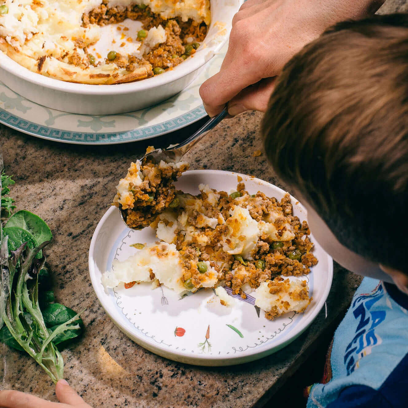 Cottage pie being spooned onto a child's dinner plate