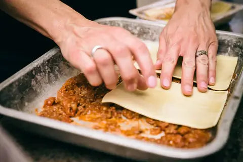 Hands layering pasta in a tray