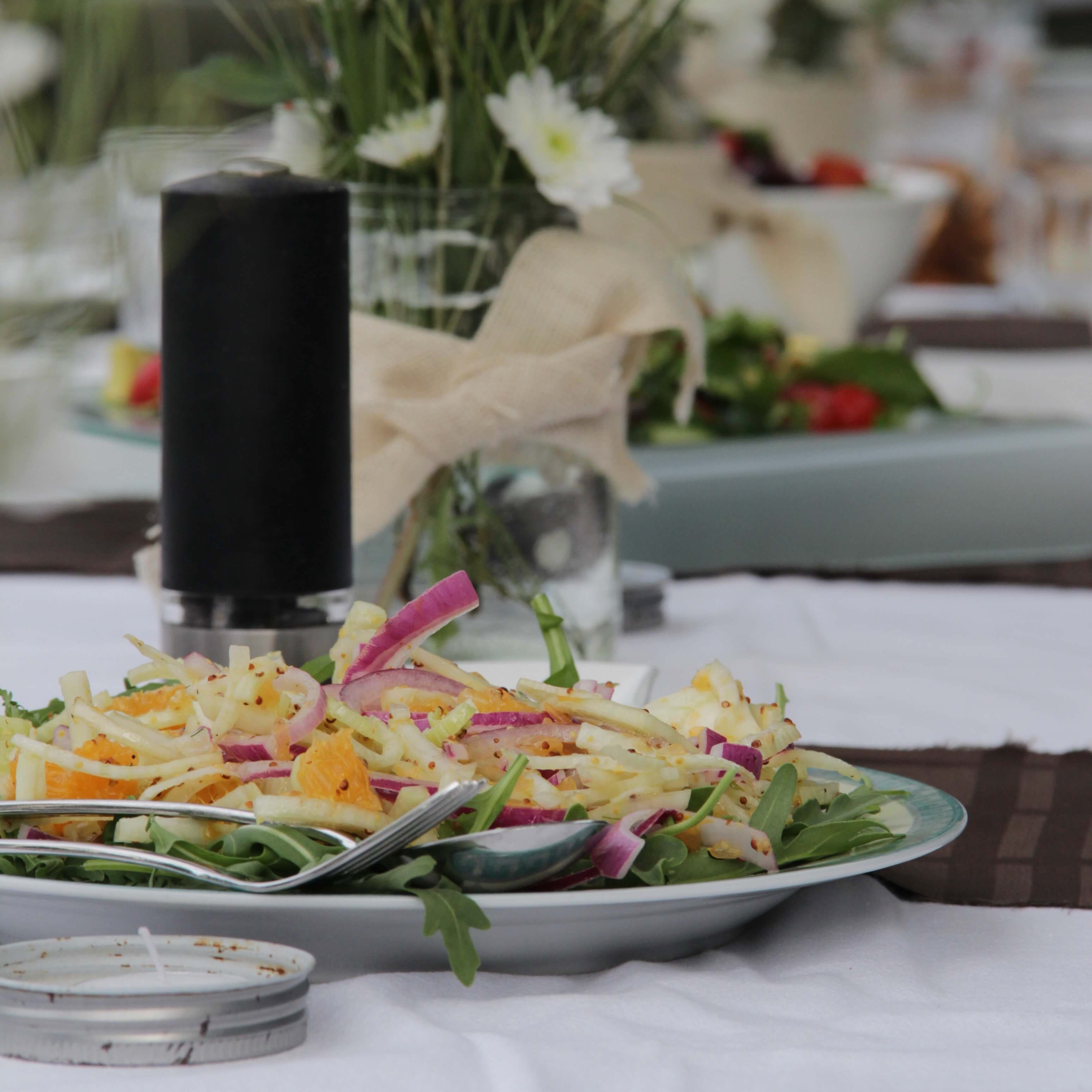 Table set for a banquet with fresh salads, florals in vases & a pepper shaker