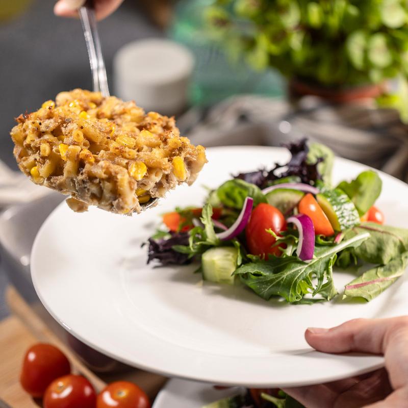 A slice of tuna pasta bake is being served onto a waiting plate. The plate already has a fresh salad on it.