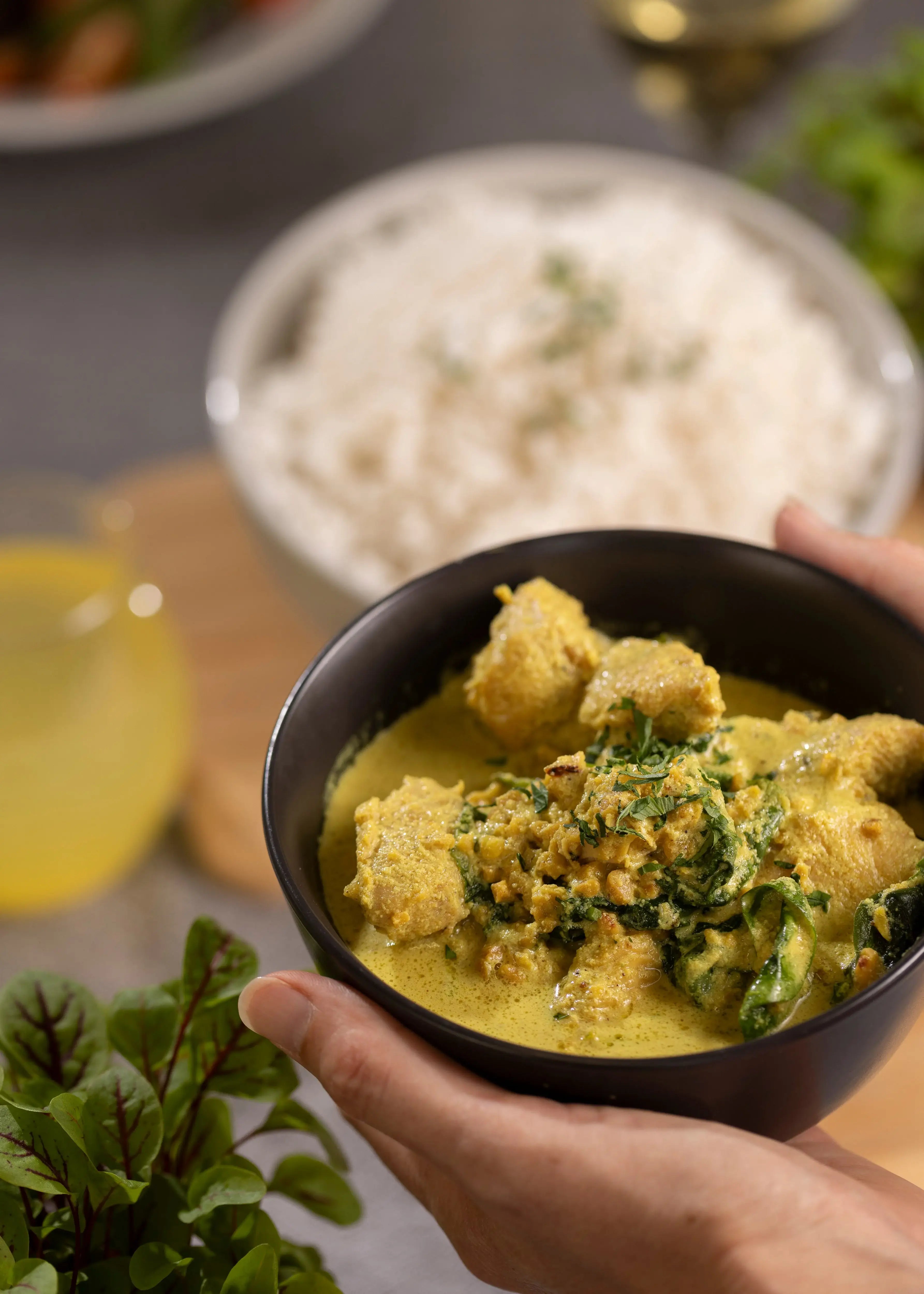 Bowl of bright yellow curry with chicken pieces and greens
