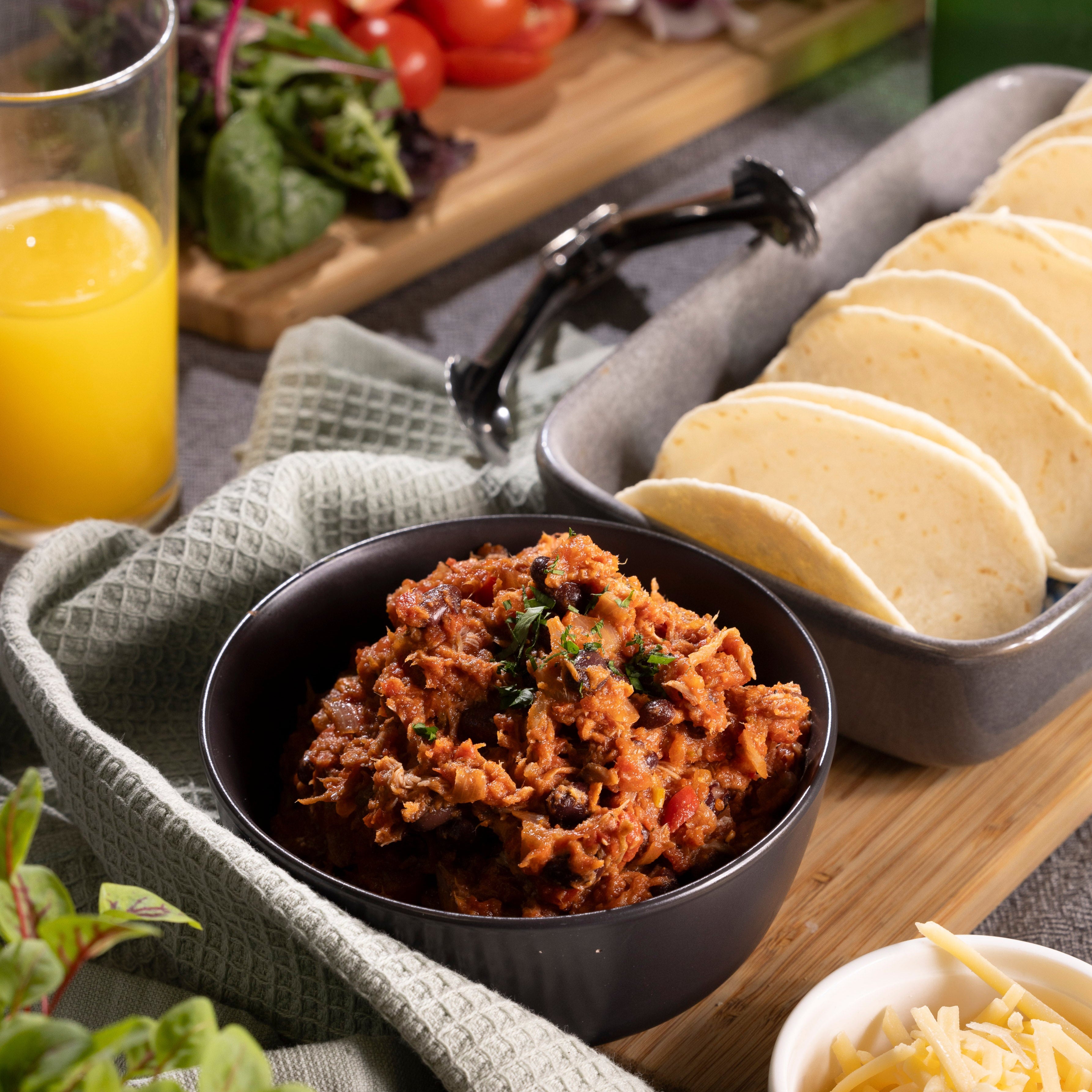 A bowl of chilli con carne in a dish with a second dish of tortillas sit on a table