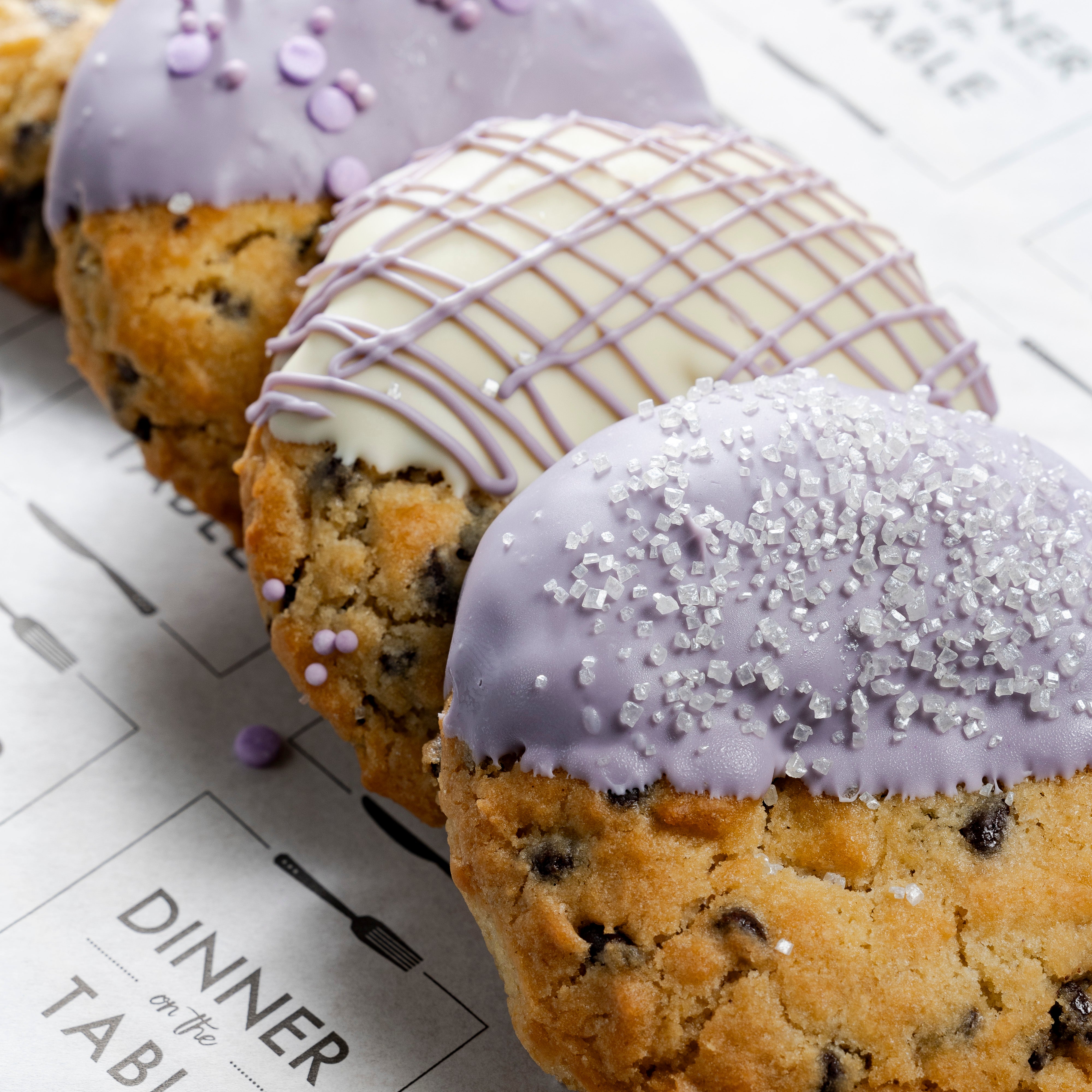 IWD cookies with various toppings in purple & white. They're stilling on Dinner on the Table printed packaging.
