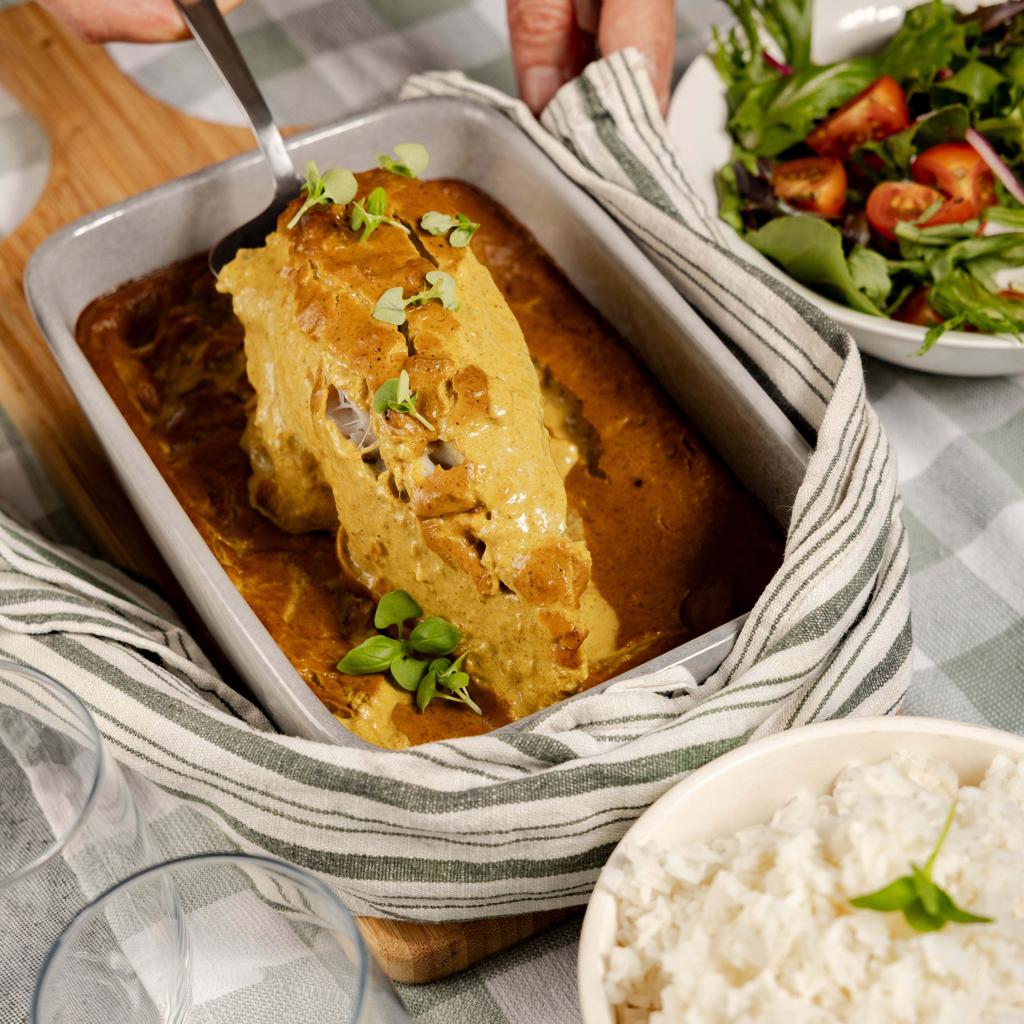 Fish being lifted out of the curry sauce with a side of salad and rice on a table.