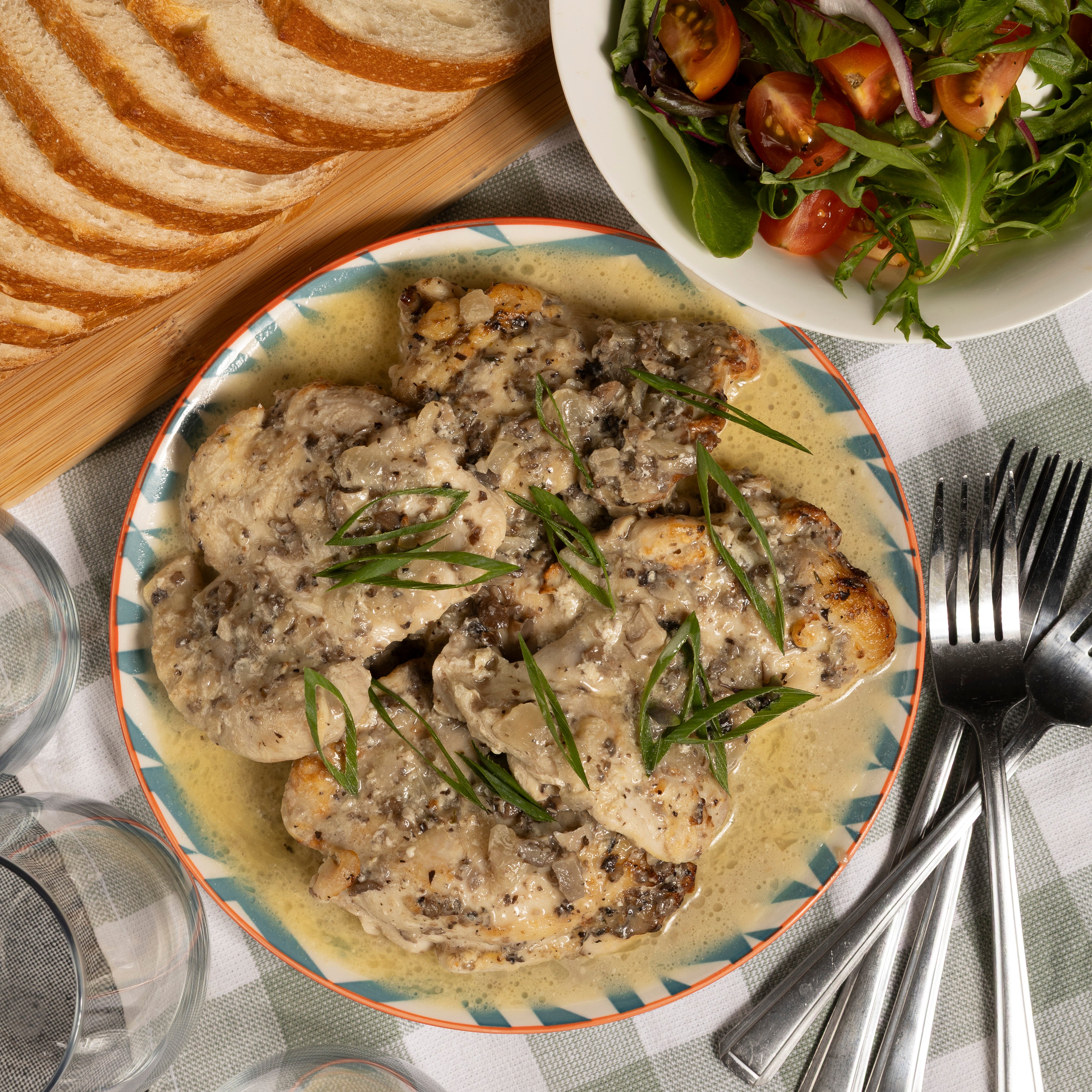Plated dish of to share  Chicken with Mushroom Medley creamy mushroom sauce with bread and salad on a checkered tablecloth