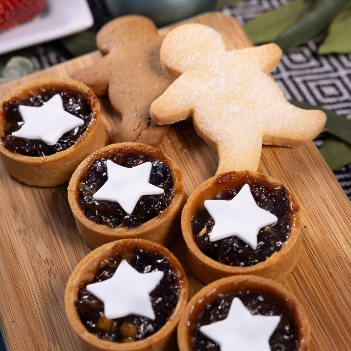 Fruit mince pies, gingerbread people and sugared shortbread sit on a wooden board.