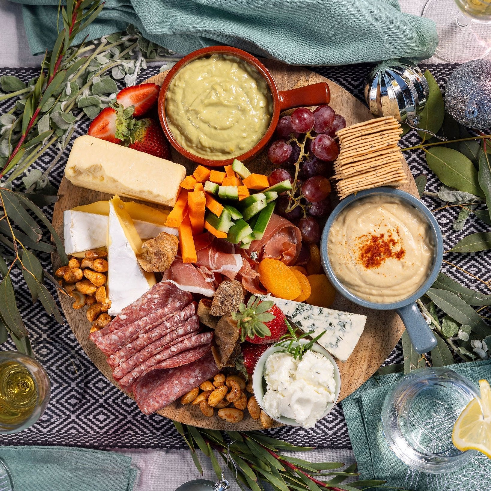 A cheese & antipasto mix sits on a wooden board on a Christmas table