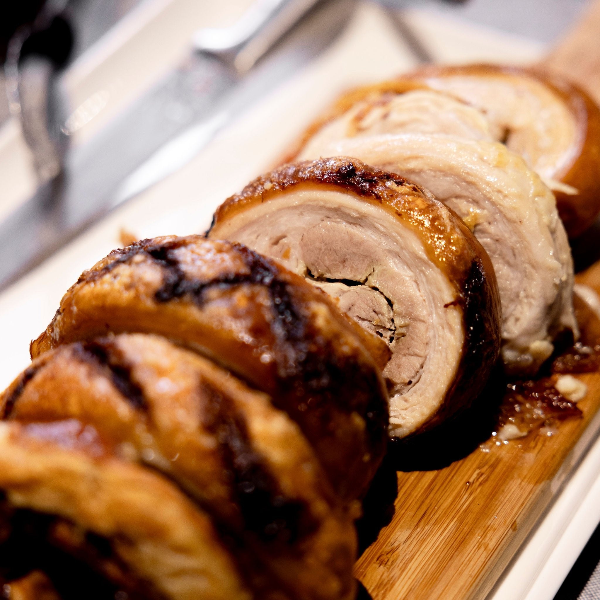 A sliced pork belly roll sits on a wooden board, ready to be served.