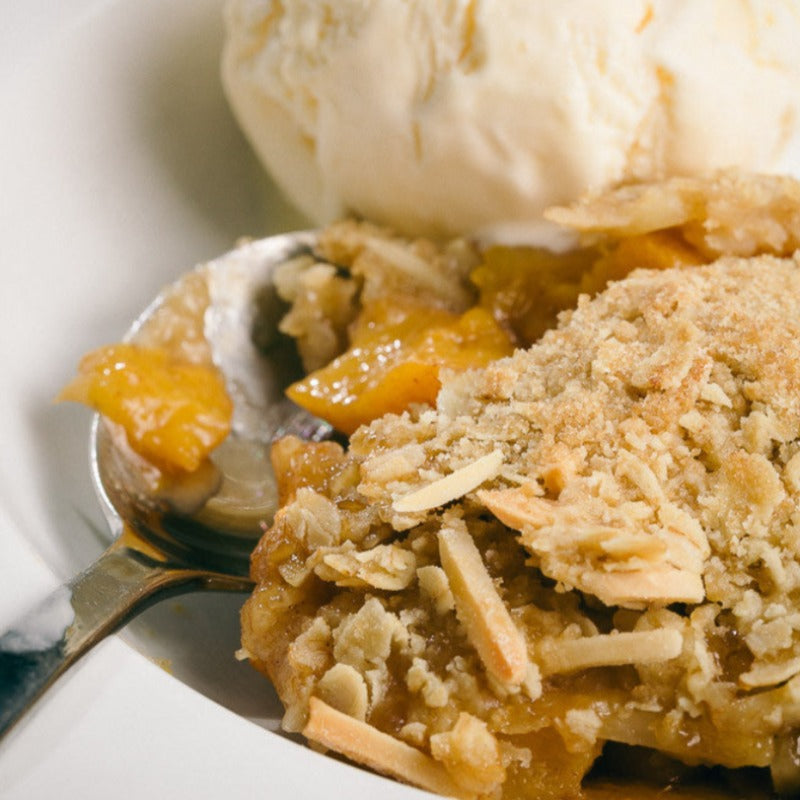 Apple & apricot crumble in a bowl with a spoon. There is a scoop of vanilla icecream in the bowl too.