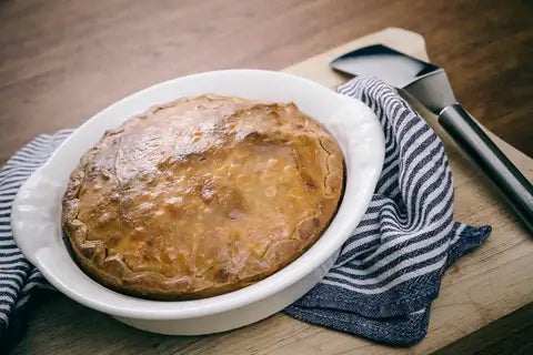 Golden baked pie in a white dish on a wooden board