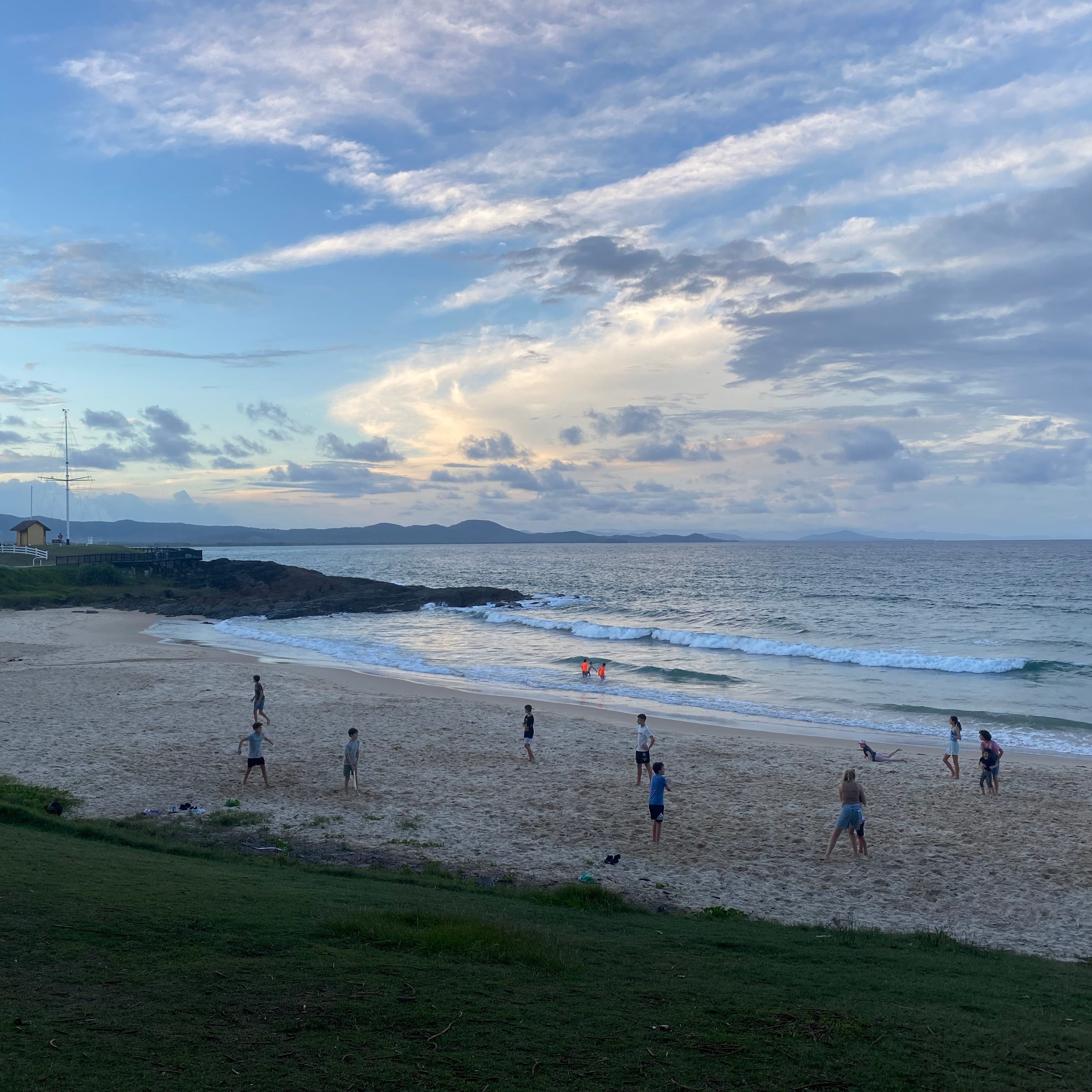 A group of people are playing cricket on the beach in the early evening