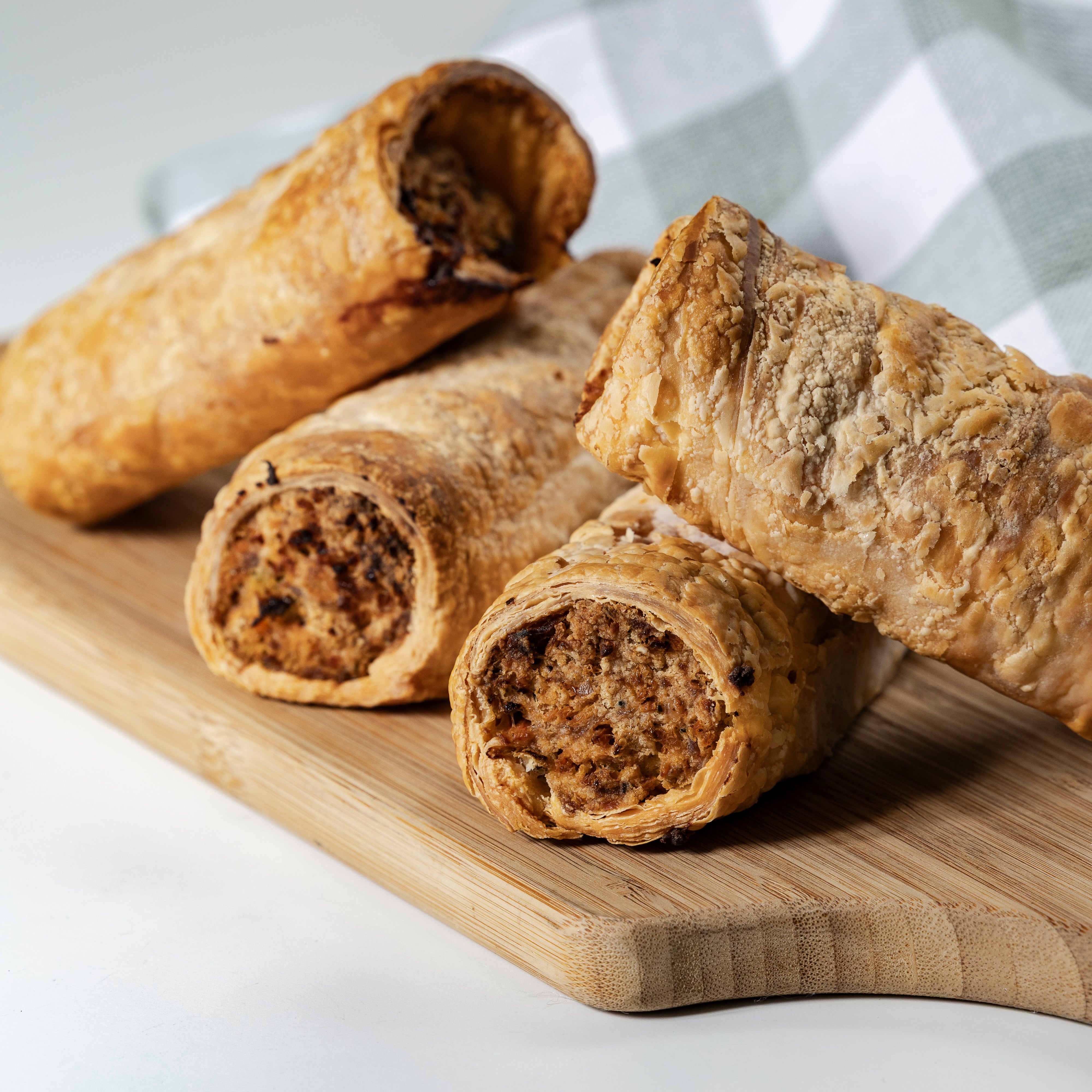 Four homemade sausage rolls sitting on a wooden board.